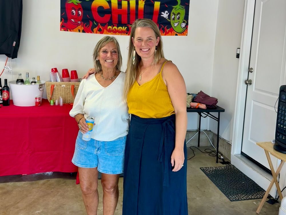 Two women standing in a garage under a chili cook-off banner