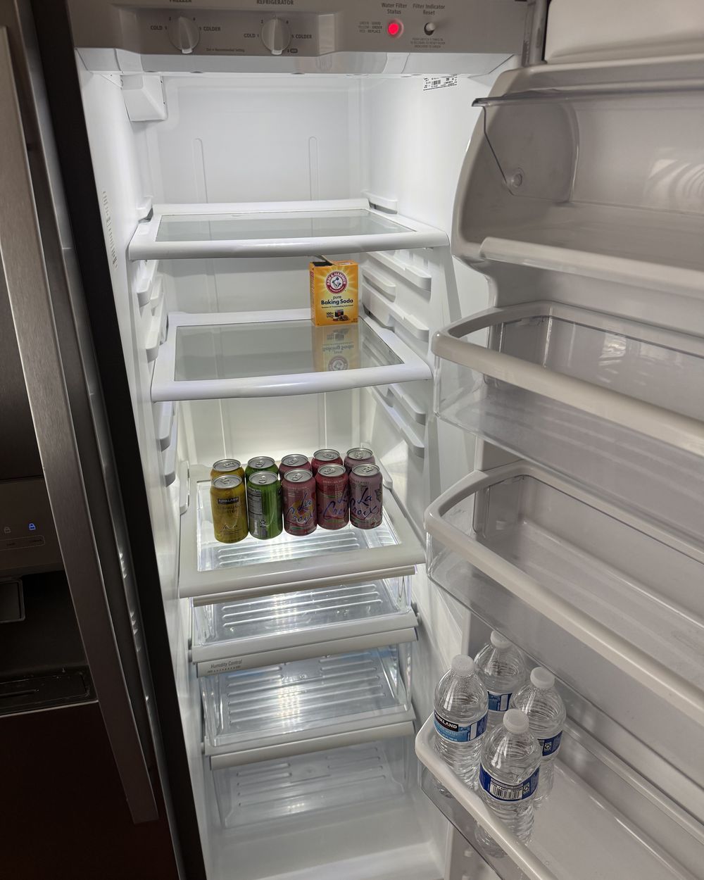 Open refrigerator in a vacant listing stocked with canned drinks and bottled water for buyers